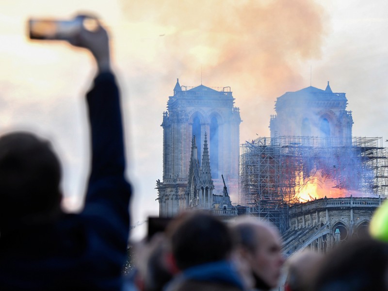 Notre-Dame in Flammen: Ein Passant in Paris fotografiert die brennende Kathedrale am Abend. 