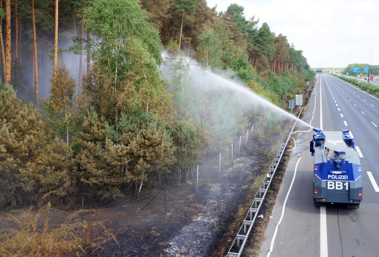 Ein Wasserwerfer der Polizei löscht am Rande eines Waldgebietes auf der Autobahn.