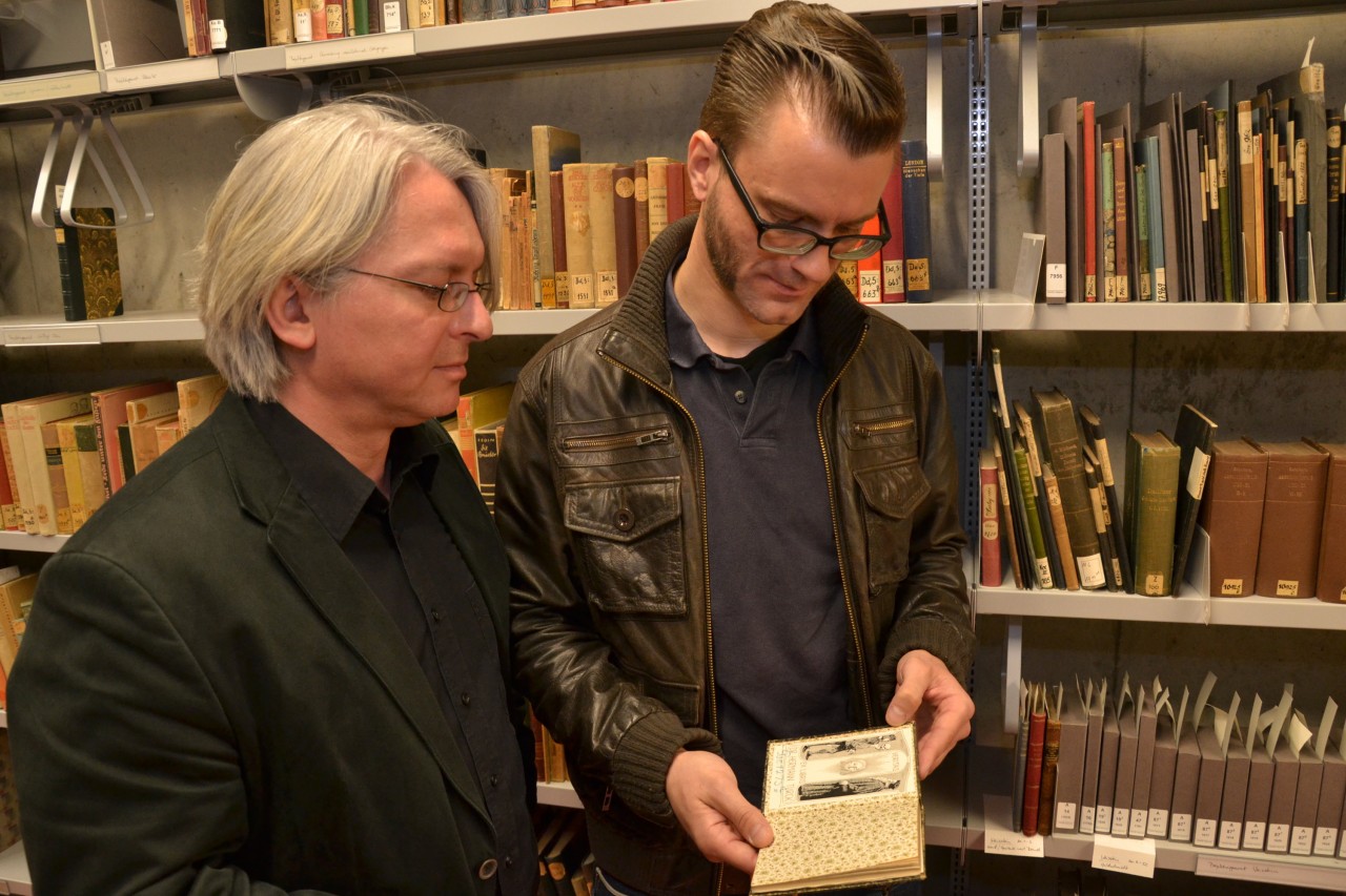 Provenienzforschern Rüdiger Haufe (l) und Sebastian Schlegel betrachten ein Buch aus der Bibliothek Hermann Türcks im Tiefenmagazin der Herzogin Anna Amalia Bibliothek in Weimar.