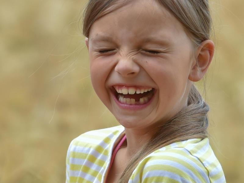 Ein Mädchen hält in einem Getreidefeld einen Blumenstrauß in der Hand und lacht.