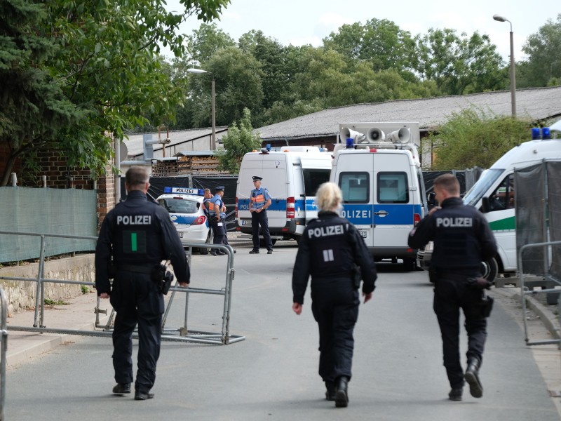 Polizisten gehen durch eine mit Absperrgittern blockierte Straße entlang. 