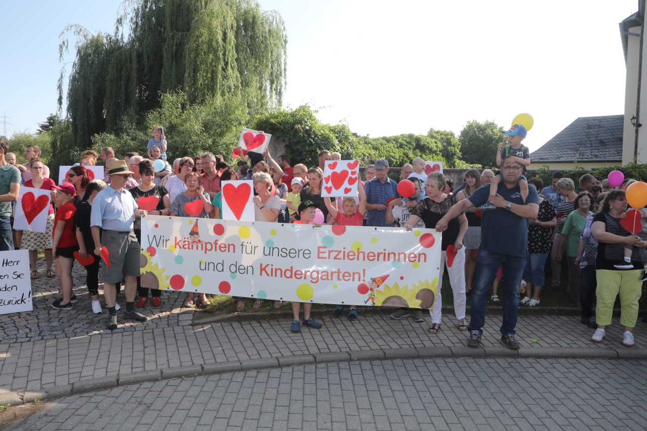 Kinder und Eltern stehen hinter ihren Erzieherinnen. 