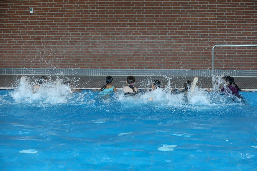 Kinder halten sich am Schwimmbecken fest und machen Übungen 