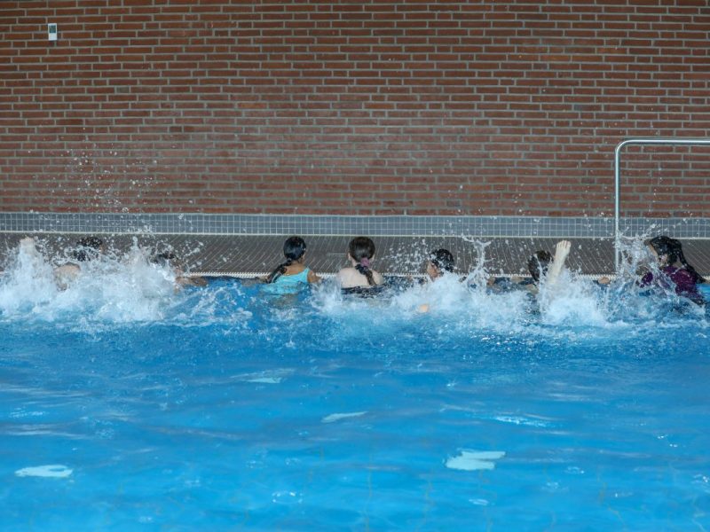 Kinder halten sich am Schwimmbecken fest und machen Übungen
