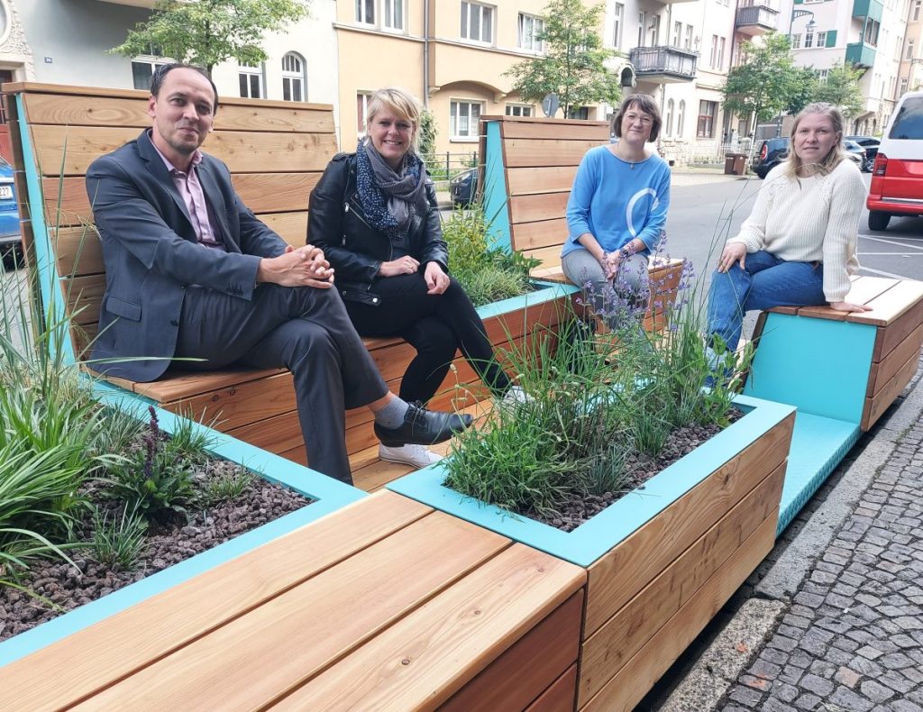 „Bürgermeister Christian Gerlitz, Cornelia Förster vom Ortsteilrat Zentrum, Ulrike Zimmermann vom Fachdienst Mobilität und Anwohnerin Nancy Droese nahmen am neu aufgestellten Parklet in der Sophienstraße Platz.“