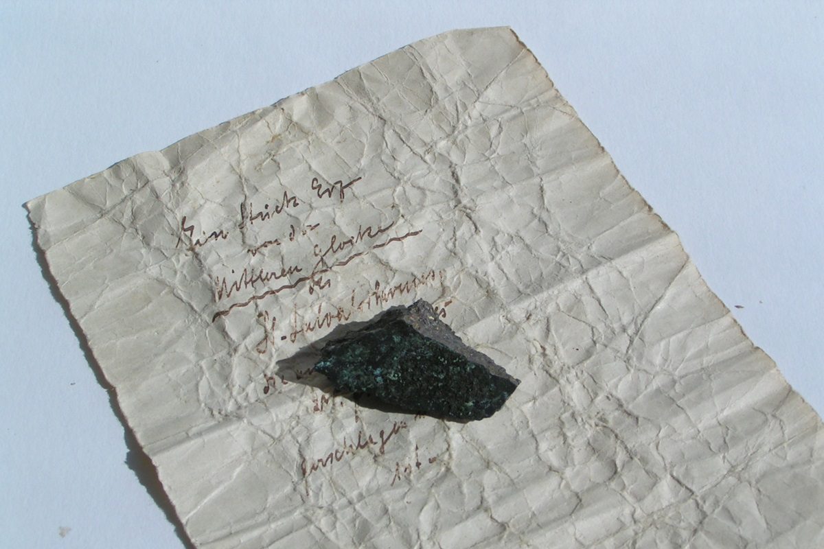 Ein Stück Papier gibt den Hinweis auf die Herkunft eines kleinen Metallstücks.