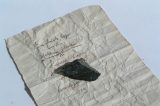 Ein Stück Papier gibt den Hinweis auf die Herkunft eines kleinen Metallstücks.