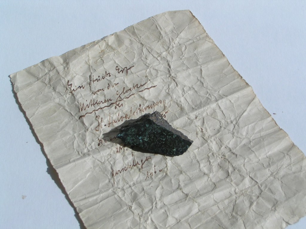 Ein Stück Papier gibt den Hinweis auf die Herkunft eines kleinen Metallstücks.